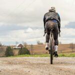 Cyclist riding a mud-covered gravel bike on a rural gravel road