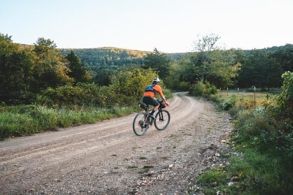 Cyclist riding a gravel road through a wooded countryside landscape